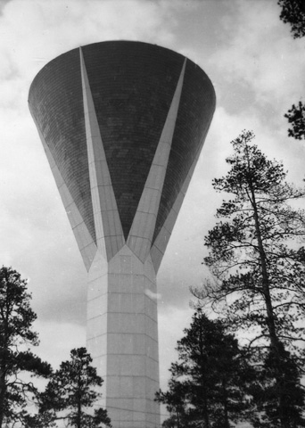 Eksteriöörikuva kartionmuotoisesta vesitornista mäntymetsän ympäröimänä.