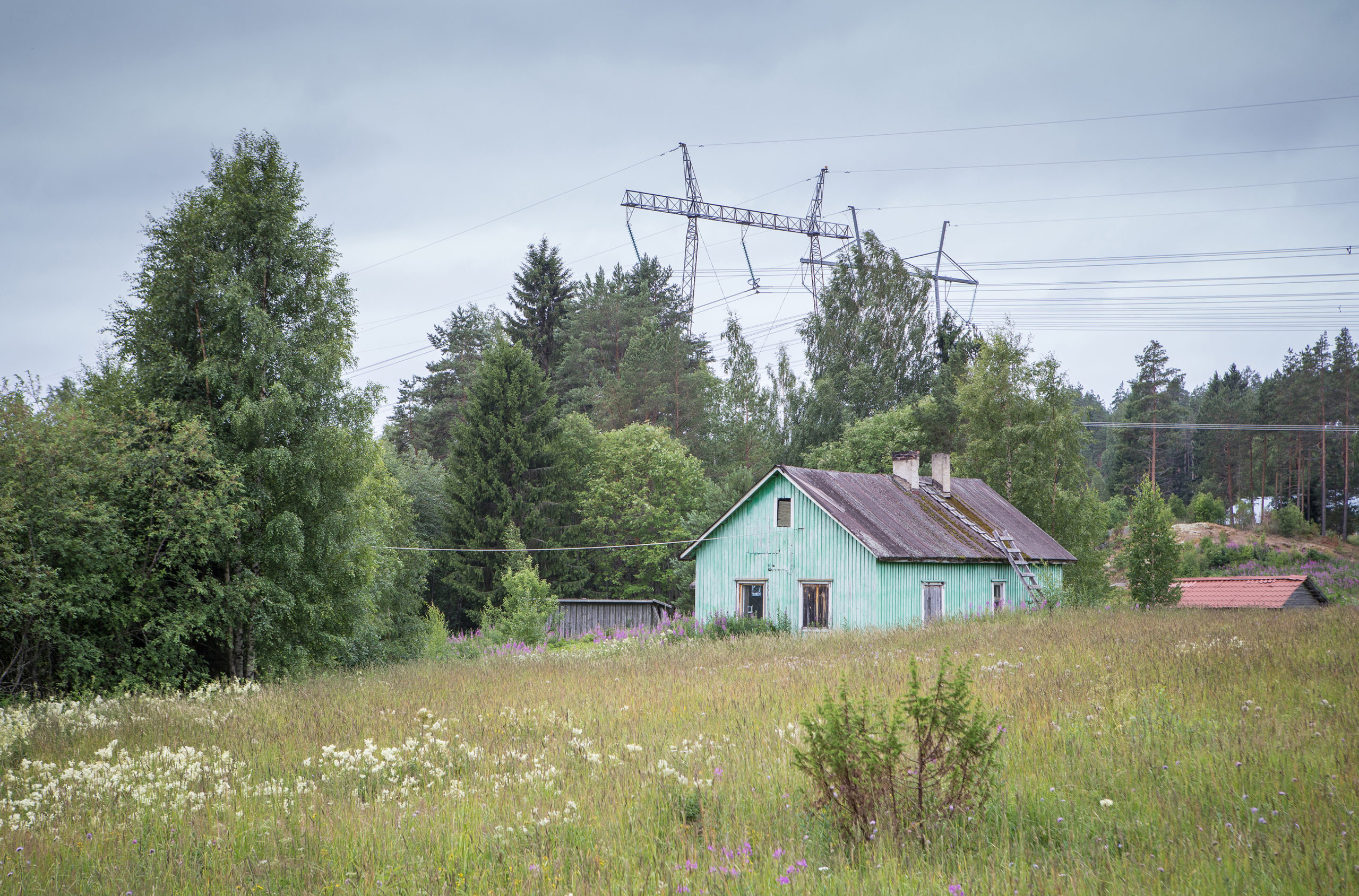 Hylätty vanha puutalo niityllä sähkölinjojen alla
